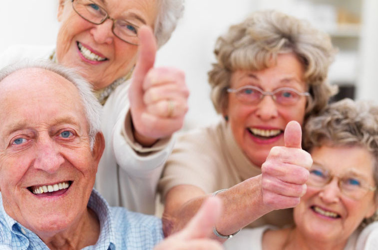 group of smiling aged men and women giving thumbs up